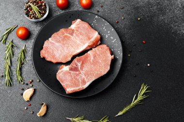 Taze ot ve sebzelerin yanında bir tabakta iki çiğ domuz pirzolası..