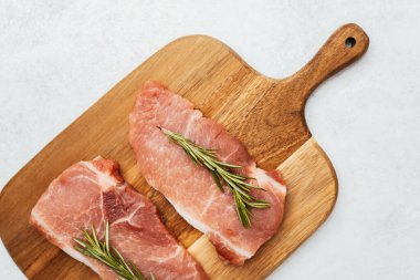 İki çiğ domuz pirzolası, ahşap kesme tahtasının üzerinde taze biberiyeyle süslenmiş..