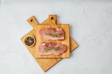 Biberiyeyle süslenmiş iki çiğ biftek baharatların yanında ahşap tahtalarda oturur..