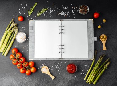 Koyu arkaplanda yemek malzemeleriyle çevrili boş sayfaları olan tarif defteri