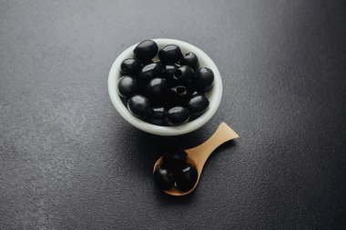 Beyaz kasede siyah zeytin ve siyah masada tahta kaşık.