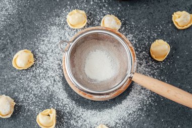 Boş süzgeç ve un tozlu yüzeyde saçılmış çiğ kapel makarna.