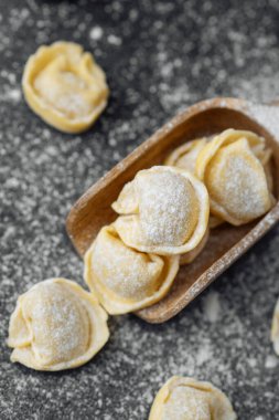Ahşap kepçeyle un kaplı koyu arkaplanda çiğ kapel makarna.