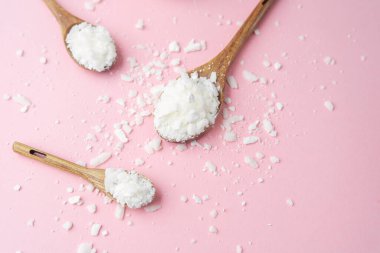 Pastel pembe arka planda soya mumu tanecikli çoklu tahta kaşıklar.