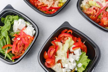 Yemek hazırlama ya da sağlıklı yemek hazırlama konsepti için içinde gurme malzemelerinin bulunduğu siyah kaplarda çeşitli taze salatalar.