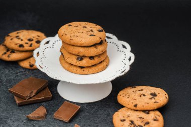 Çikolata parçalı kurabiyeler, etrafını çikolata parçalarıyla çevrili beyaz bir stantta düzenlenir..