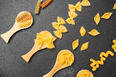 Koyu bir yüzeye karşı tahta kaşıklarda farklı şekillerde ve renkte makarna sergilenir..