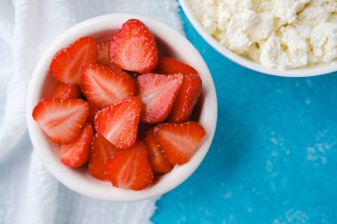 Bir kase süzme peynir ve dilimlenmiş çilek mavi desenli arka planda