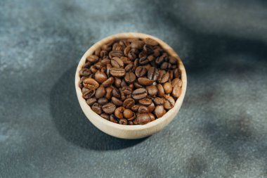 Koyu arka planda yaprak gölgesi olan tahtadan bir kasede kahve çekirdeği.