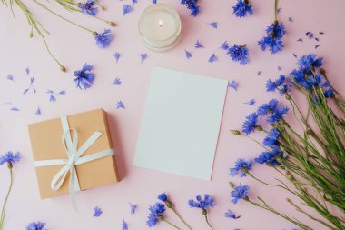 Mumlu kart, hediye kutusu ve pembe arka planda çiçek.