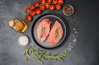 Siyah seramik tabakta çiğ biftek, biberiye, kiraz, domates, tuz ve biber.