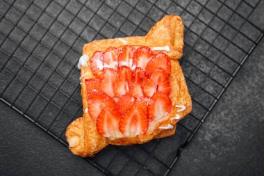 Üzerine taze dilimlenmiş çilek serpilmiş krema serpiştirilmiş gevrek hamur işi..