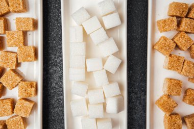 Dikdörtgen tabakalarda sıralanmış çeşitli şeker küpleri farklılıklarını vurgular.