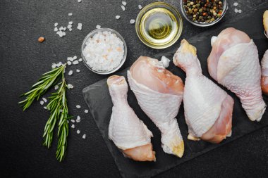 Siyah tahta üzerine yerleştirilmiş tavuk budu, otlar ve tuzlu.