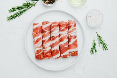 Jambona sarılmış sosis, beyaz tabakta otlar ve yağla birlikte.