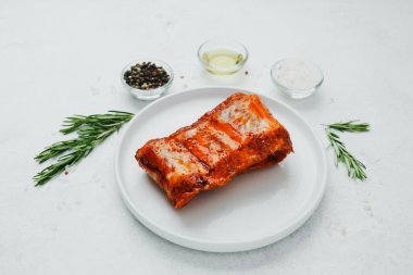 Beyaz tabakta marine edilmiş domuz pirzolası, biberiye ve baharatlı.