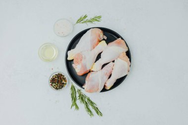 Biberiye ve baharatlı siyah tabakta çiğ tavuk budu.