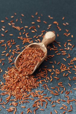 Kırmızı pirinçle dolu ahşap kepçe siyah arka planda dökülüyor.