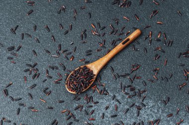 Koyu arka planda siyah pirinçli ahşap kaşık ve dağınık taneler.