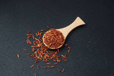 Kırmızı pirinçle dolu ahşap kaşık ve dağılmış tahıllar siyah sırtüstü