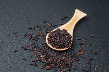 Siyah pirinçle dolu tahta kaşık ve koyu arkaplana dökülen tahıllar.