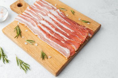 Ahşap tahtada çiğ pastırma dilimleri, biberiye ve koyu arkaplanda tuz.