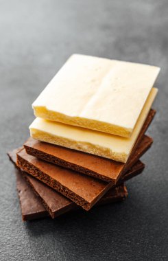 Siyah zemin üzerinde beyaz, süt ve koyu aromalı çeşitli çikolata parçaları yığını