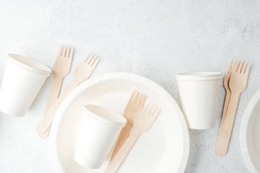 Beyaz tek kullanımlık tabaklara dağılmış beyaz kağıt bardaklar ve ahşap çatallar.