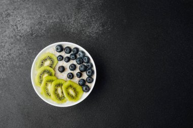 Koyu arkaplanda kivi dilimleri ve yaban mersinli sağlıklı kahvaltı kasesi.