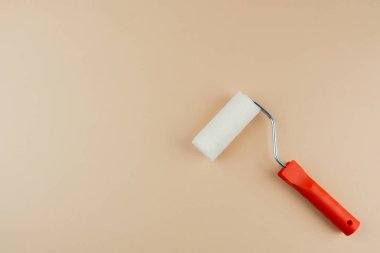 Ev dekorasyonu ve DIY boyama konsepti için bej arka planda kırmızı saplı boya silindiri