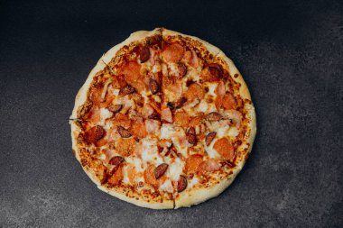 Biberli ve sosisli yeni pişmiş bir pizza siyah bir yüzeye oturur..