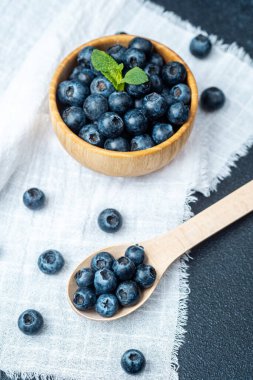 Dolgun yaban mersinleri bir kaşığın yanındaki ahşap kasede sergilenir, tazeliği arttırır..