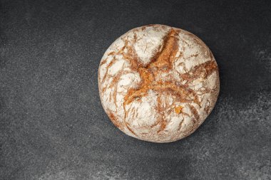 Sıcak ve kabuklu ekmek dilimlenmeye hazır karanlık bir yüzeyde dinleniyor..