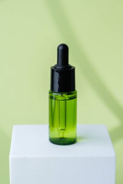 Yeşil kozmetik şişesi beyaz küp kaidesi üzerinde sergilenir