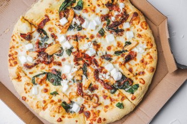 Ispanak, peynir, tavuk ve karton kutuda kurutulmuş domatesli pizza.