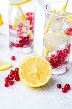 İki uzun bardakta limon kırmızısı üzümlü su ve sarı çizgili kamışlı beyaz masa!