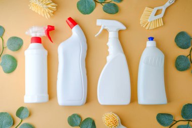 Soluk arkaplanda yeşil yapraklı beyaz temizlik şişeleri ve fırçalar..