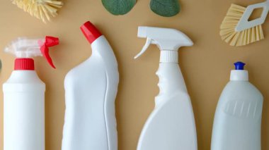 Açık kahverengi yüzeye yerleştirilmiş beyaz temizlik şişeleri ve fırçalar.