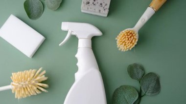 Yeşil bir yüzeyde yapraklarla temizlenmiş fırça ve süngerlerle dolu beyaz sprey şişesi.