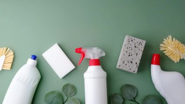 Şişeler ve süngerler gibi, soluk yeşil arka planda yapraklarla sıralanmış temizlik malzemeleri..