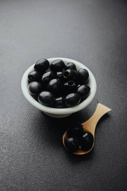 Beyaz kasede siyah zeytin ve siyah masada tahta kaşık.