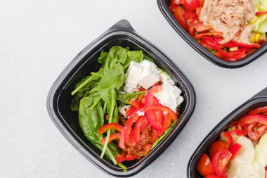 Yemek hazırlama ya da sağlıklı yemek hazırlama konsepti için içinde gurme malzemelerinin bulunduğu siyah kaplarda çeşitli taze salatalar.