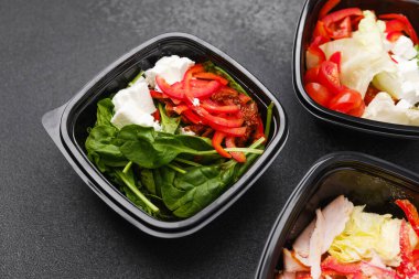 Yemek hazırlama ya da sağlıklı yemek hazırlama konsepti için içinde gurme malzemelerinin bulunduğu siyah kaplarda çeşitli taze salatalar.