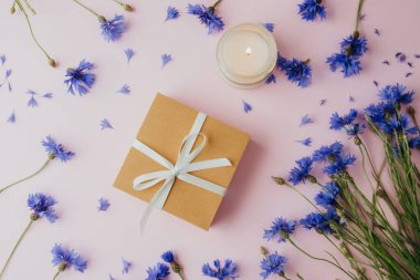 Mumlu hediye kutusu ve pembe arka planda çiçek.