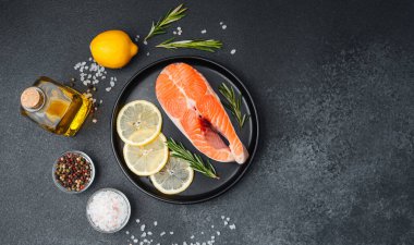 Limon dilimleri ve koyu bir yüzeyde otlarla süslenmiş taze somon filetosu..