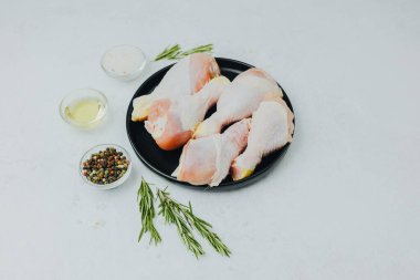 Biberiye ve baharatlı siyah tabakta çiğ tavuk budu.