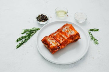 Beyaz tabakta marine edilmiş domuz pirzolası, biberiye ve baharatlı.