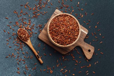 Tahtadaki ahşap kasede kırmızı pirinç dağınık tanecikler ve kaşıkla.