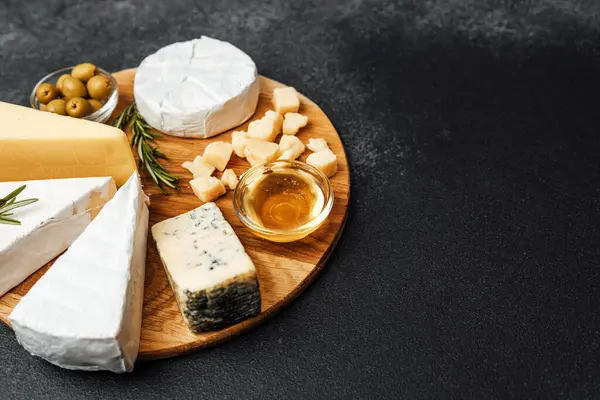 İçinde çeşitli peynirler, zeytinler ve bal bulunan güzel düzenlenmiş bir peynir tabağı..