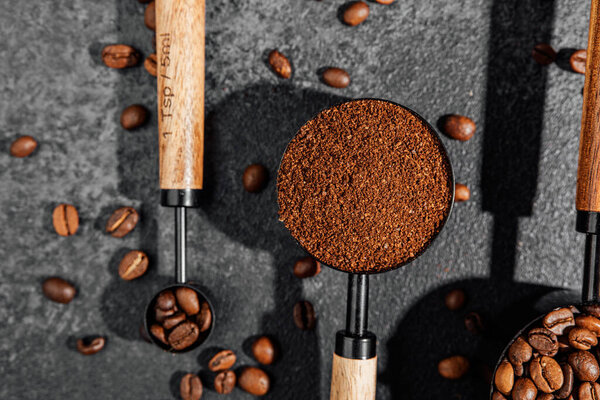 Ground coffee, instant coffee and beans in wooden bowl and scoops on textured background